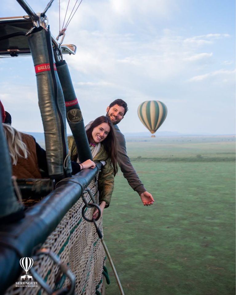 Hot air balloon flying over Serengeti plains with wildlife herds visible below at sunrise in Tanzania