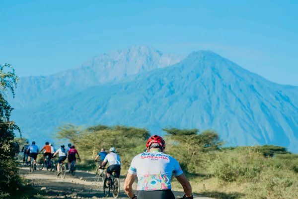 Cyclists riding through Tanzania’s countryside with Mount Kilimanjaro visible in the background.