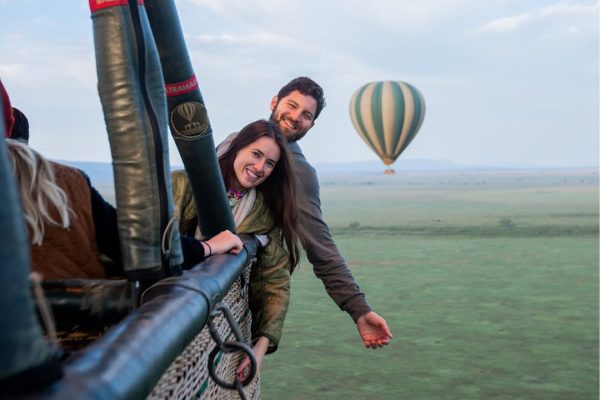 Hot air balloon flying over Serengeti plains with wildlife herds visible below at sunrise in Tanzania